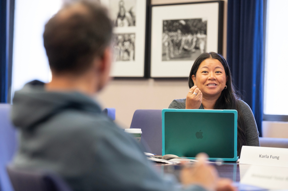 Smiling woman with turquoise laptop speaking to colleague across a conference table