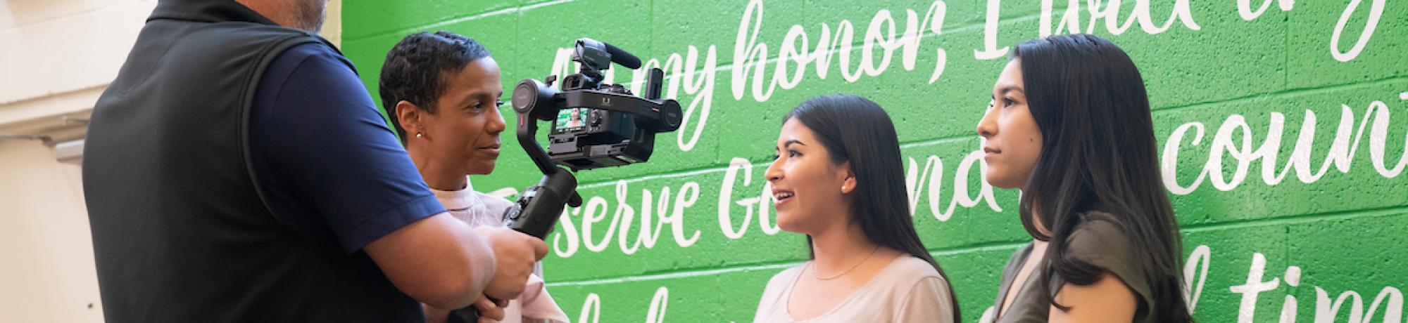 video producer filming students against green wall