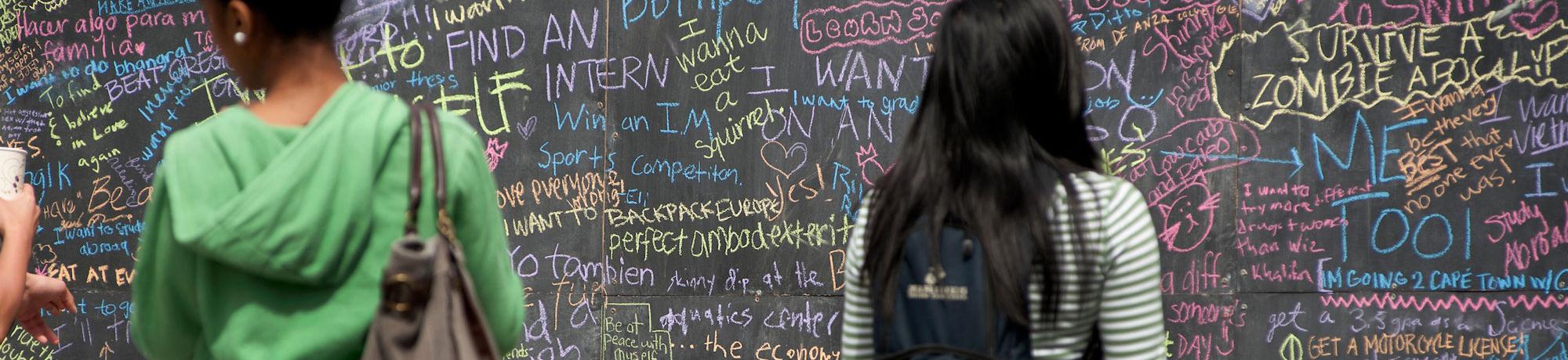 Students write things they would like to do before they graduate on a publicly mounted chalkboard